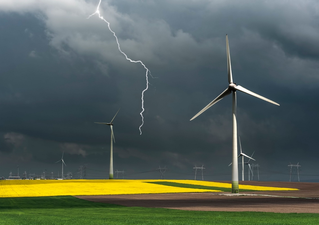 Several wind turbines are positioned across mutiple fields. The sky is very dark and stormy, and a lightning bolt is visible.