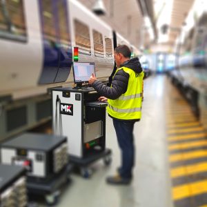 A production technican at a train manufacturing plant is operating a test system whilst giving a 'thumbs up' hand gesture