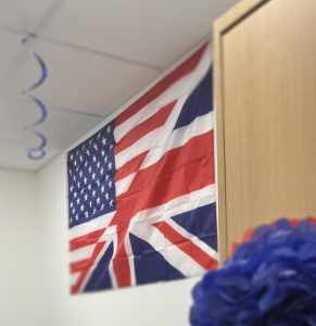 A flag hangs from a wall , with blue and red party decorations surrounding it. The flag is a combination of the British Union Jack split diagonally with the United States of America flag.