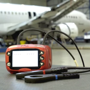 ExLRT tool is positioned on a table in the foreground, with the couplers and probes in front of it. In the background is a plane in a maintenance hangar.